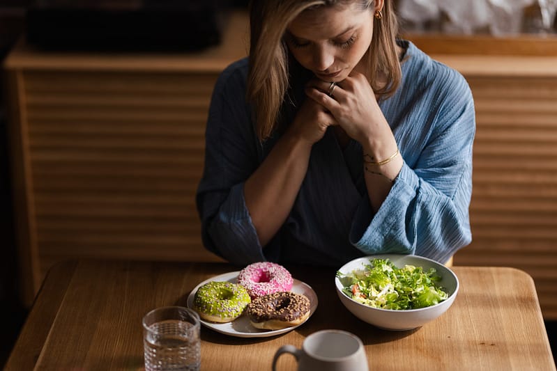 a woman struggling between eating a salad or donuts, showing how important medical billing for eating disorder treatment centers is